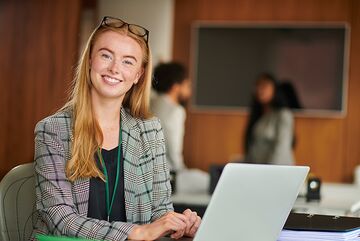 Eine Studentin sitzt in einem Unterrichtsraum mit ihrem Laptop