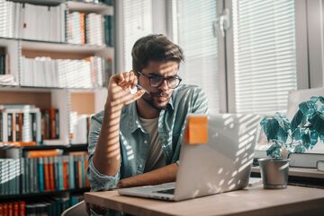 Studierender sitzt am Tisch mit Laptop und Lernmaterial, arbeitet konzentriert in heller, moderner Umgebung.