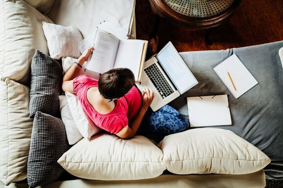 Schwangere auf dem Sofa mit Laptop und Unterlagen