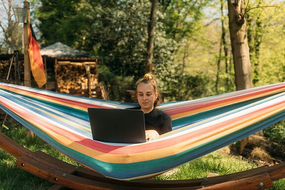 Junge Frau sitzt mit ihrem Laptop in einer Hängematte im Wald