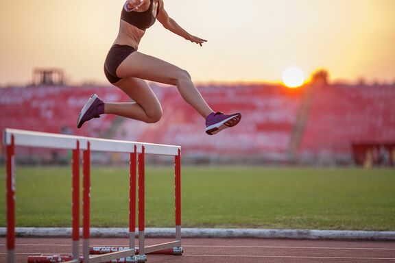 Frau springt auf Sportplatz über eine Hürde