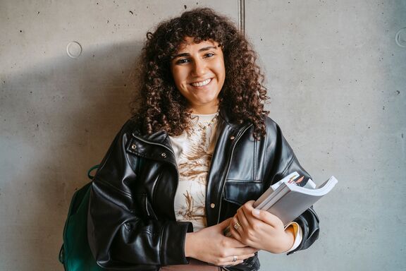 Portrait einer lachenden Studentin mit Studienunterlagen