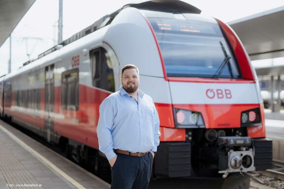 Mann steht auf Bahnsteig vor einem Zug der ÖBB und blickt in die Kamera.