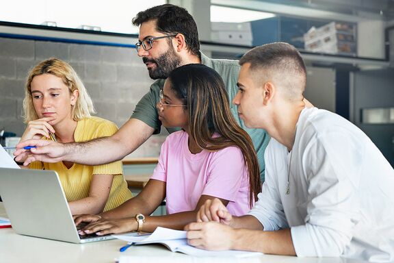 drei Studierende und ein Lehrender an einem Tisch mit Laptop