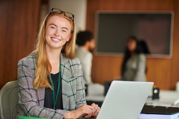 Eine Studentin sitzt in einem Unterrichtsraum mit ihrem Laptop
