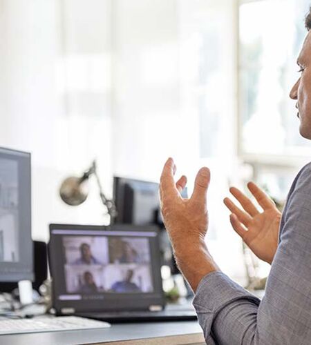 Mann im Rollstuhl, von hinten zu sehen, sitzt an Tisch vor Bildschirm und interagiert während eines Webinars.