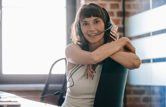 Frau mit Headset lächelt am Arbeitsplatz in Kamera