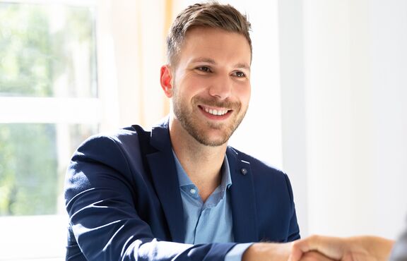 Mann lächelt beim Handschlag einer anderen Person zu, deren Hinterkopf man sieht.