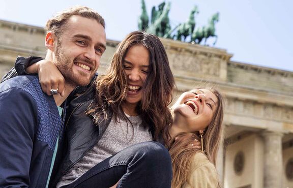Zwei Damen und ein junger Mann glücklich vor dem Brandenburger Tor