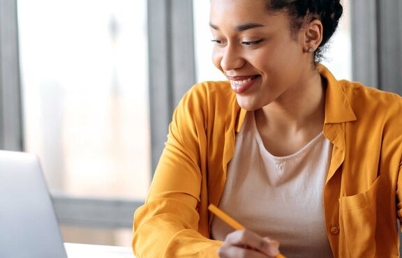 Studentin arbeitet gut gelaunt am Laptop mit Unterlagen 