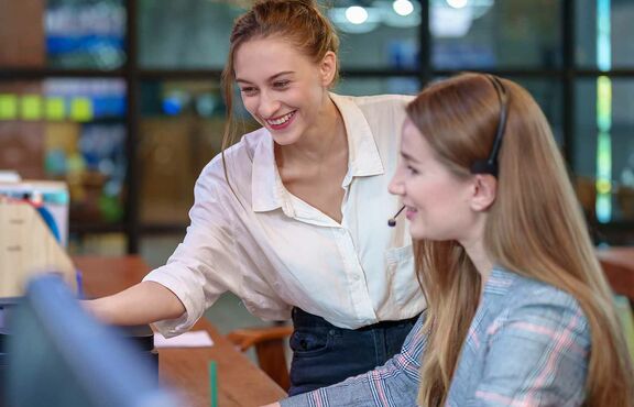 Zwei Frauen blicken auf Bildschirme und diskutieren
