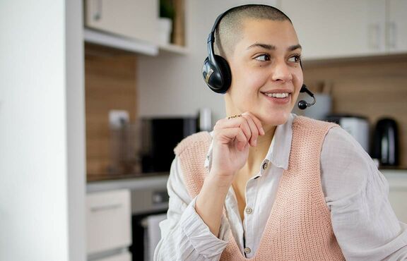 Junge Frau mit Kopfhörern sitzt an Tisch und blickt zur Seite