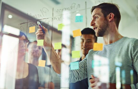 Mann erklärt einer Gruppe von Leuten Grafik an einer Tafel.