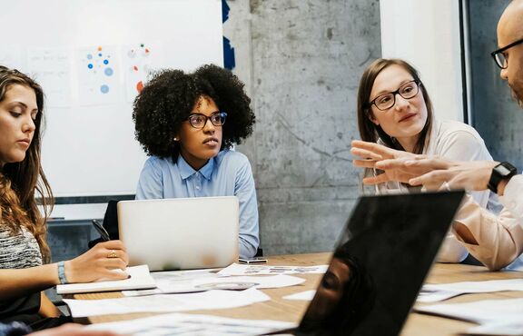 Fünf junge Forschende sitzen an einem Tisch und diskutieren