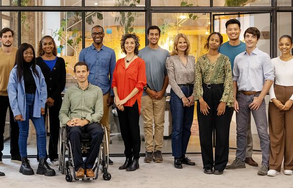 Eine Gruppe vielfältiger Menschen steht in einem Büro und lächelt in die Kamera.