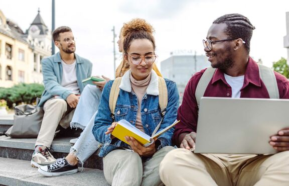 Junge Menschen sitzen gemeinsam auf einer Treppe, unterhalten sich und lernen.