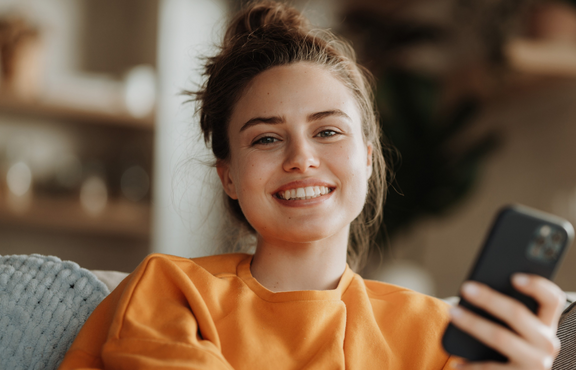 Junge Frau sitzt auf dem Sofa und schaut fröhlich aus