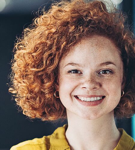 junge Frau mit roten Locken lacht in die Kamera