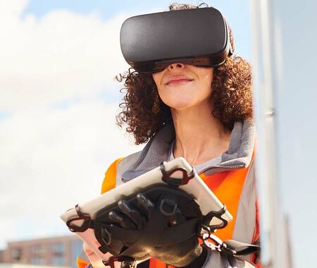 Frau testet gut gelaunt mit Tablet in der Hand eine VR-Brille 
