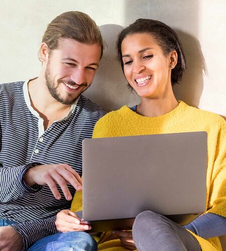 Frau und Mann sitzen an Wand gelehnt und schauen auf Notebook