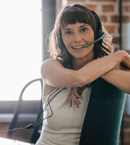 Frau mit Headset lächelt am Arbeitsplatz in Kamera