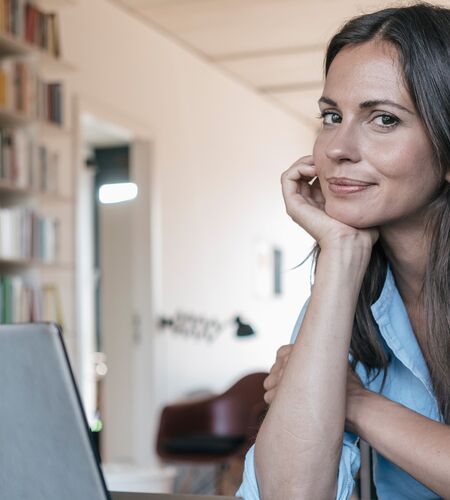 Junge Frau mit Hand unter dem Kinn vor einem Laptop