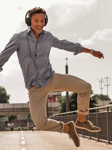 Mann auf Brücke mit Kopfhörern und Aktentasche springt freudig in die Luft