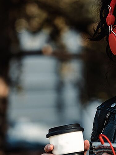 Dunkelhaarige Frau mit roten Kopfhörern hört über ihr Smartphone