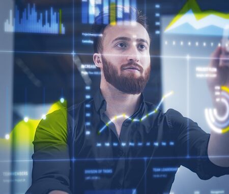 Mann in dunklem Hemd steht vor transparentem Bildschirm mit bunten Daten- und Diagrammanzeigen.