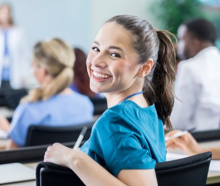 Mehrere Studierende sitzen in einem Hörsaal, eine Person in blauer Kleidung sitzt im Vordergrund und hält einen Stift.