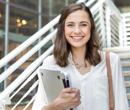 Junge Frau mit Tablet steht auf Treppe und blickt in Kamera.