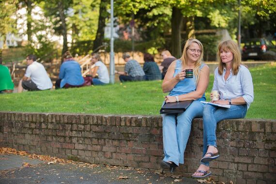 Zwei Frauen auf einer Steinmauer sitzend, Kaffee trinkend