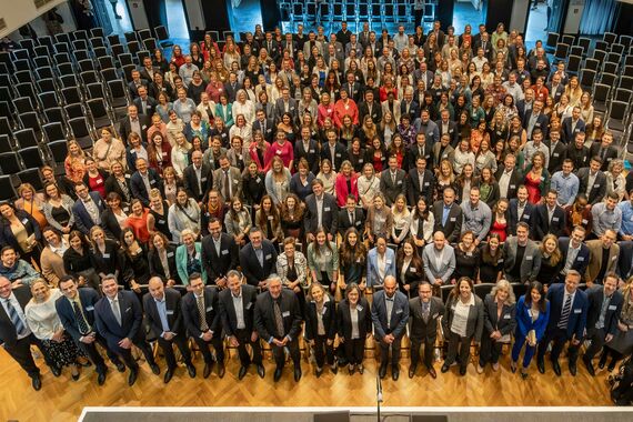 Bild mit großer Gruppe von Hochschulabsolvent:innen während Abschlussfeier, von schräg oben fotografiert.