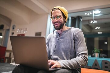 Mann mit Mütze sitzt vor Notebook und lächelt