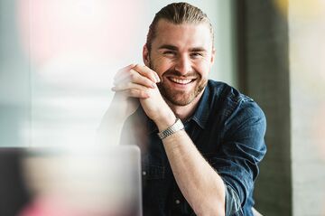Mann mit Zopf am Schreibtisch lächelnd