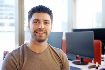 Junger Mann sitzt im Büro vor einigen Monitoren