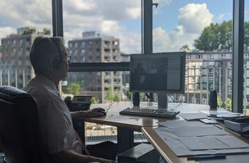 Mann sitzt am Fenster am PC und nimmt an Online-Konferenz teil 