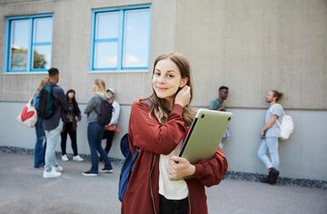 Junge Frau mit Notebook auf Schulhof, die sich die Haare hinter die Ohren macht