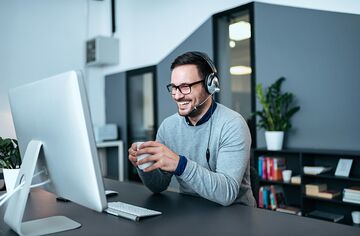 bärtiger Mann mit Headset und Kaffeetasse sitzend vor Bildschirm 