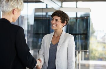 Zwei Frauen im Business-Umfeld schütteln Hände und lächeln