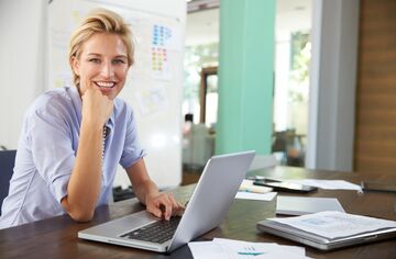 Blonde, lächelnde Frau am Schreibtisch vor einem Laptop sitzend