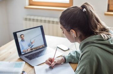 Junge Frau sitzt am Schreibtisch vor einem Computer und schreibt auf einen Block