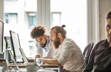 Zwei junge Männer sitzen vor Notebooks und diskutieren