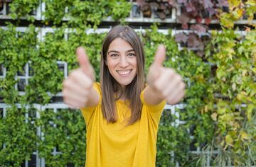 Junge Frau in gelbem Shirt reckt beide Daumen in die Höhe