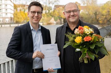 Prof. Dr. Lars Binckebanck überreicht Prof. Dr. Florian Oldenburg-Tietjen die Ernennungsurkunde und einen Blumenstrauß.