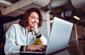 Eine Frau sitzt lächelnd vor einem Laptop.