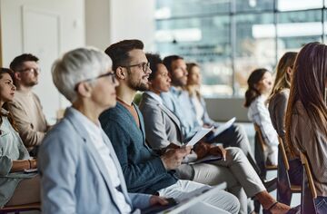 Menschen sitzen in Stuhlreihen auf einer Konferenz und hören einen Vortrag