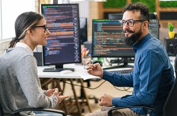 zwei Personen vor mehreren Monitoren mit Code diskutieren miteinander