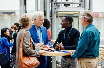 HFH ist Akademischer Partner der ICEDU 2025 Vier Personen stehen auf einer Konferenz an einem Stehtisch und unterhaltgen sich.