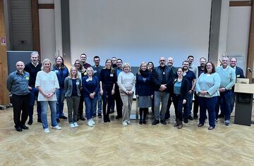 Gruppenbild mit 24 Personen in Veranstaltungsraum
